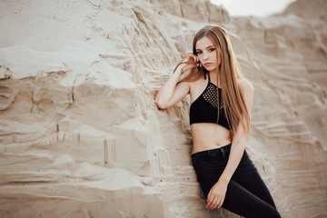 Portrait of a beautiful girl with long hair on the sands in the desert at sunset. Girl model in black jeans and top