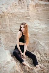 Portrait of a beautiful girl with long hair on the sands in the desert at sunset. Girl model in black jeans and top