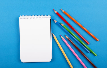 Colored pencils and notebook on blue background. Back to school concept.