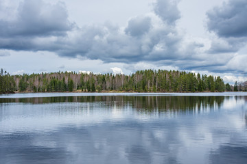 Forest on the shore of lake with cloudy sky above, reflected in the water. Taken along the Bergslagsleden hiking trail, in nature reserve Ånnaboda in central Sweden.