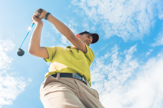 Low-angle view of a professional player wearing golf outfits while holding the club ready for the strike during individual game outdoors against cloudy sky