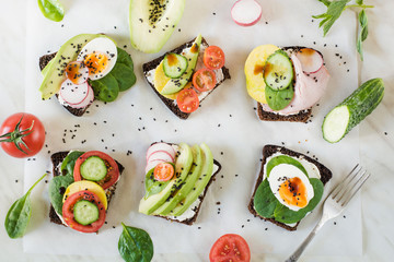 Different sandwiches with vegetables, eggs, avocado, tomato, rye bread on light marble table. Top...