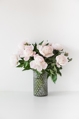 Fototapeta na wymiar Bouquet of tender pink peonies in vase near white wall