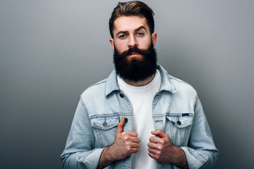 Handsome fashionable young European male with thick beard wearing trendy denim jacket, staring at...