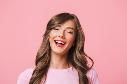 Image closeup of cheerful european woman 20s with long curly hairstyle and evening makeup laughing while looking at you with happy look, isolated over pink background