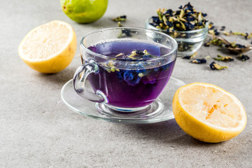 Healthy drinks, organic blue butterfly pea flower tea with limes and lemons, grey concrete background copy space