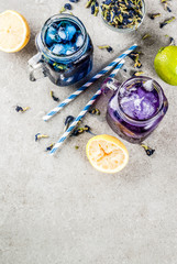 Healthy summer cold beverage, iced organic blue and violet butterfly pea flower tea with limes and lemons, grey concrete background copy space top view