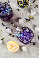 Healthy summer cold beverage, iced organic blue and violet butterfly pea flower tea with limes and lemons, grey concrete background copy space top view