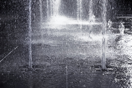 Water jets of a modern fountain on a stone pavement - toned image