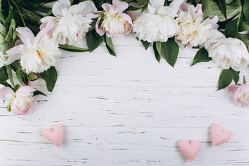 Fototapeta premium White peonies and pink hearts on a wooden background. Copy space and flat lay.