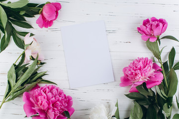 Pink and white peonies around sheet of paper on a wooden background. Copy space and flat lay.