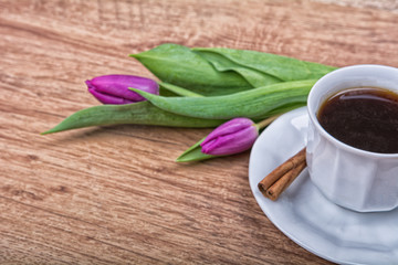 A cup of tea with cinnamon and purple tulip on a table