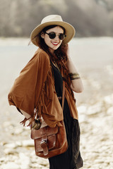 stylish hipster boho woman smiling in sunglasses with hat, leather bag, fringe poncho and...