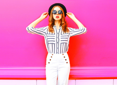 Fashion pretty woman model wearing black hat sunglasses white pants over colorful pink background