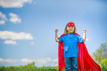 Fototapeta premium Funny little girl playing power super hero over blue sky background. Superhero concept.