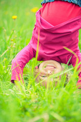 Happy little girl standing upside down on green grass in summer park