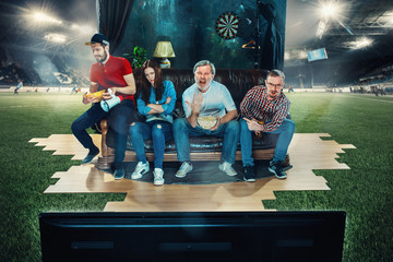 Soccer football fans sitting on the sofa and watching TV in the middle of a football field.
