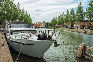 Boat moored on wide canal margin under sunny blue sky in the City Center of Weesp. Quiet and pleasant village full of canals and green near Amsterdam. Northern Netherlands.