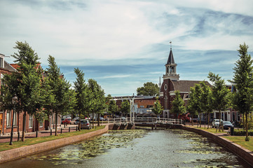 Tree-lined canal with bascule bridge, church and brick houses in street on the banks on sunny day...
