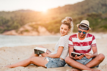 Young couple sitting at the beach and reading a book