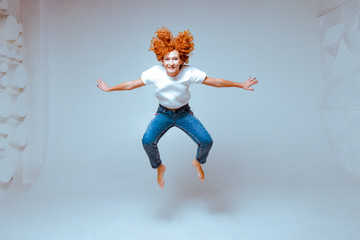 Beautiful sexy red hair smiling woman wearing high waist jeans and white t-shirt, high heels posing in studio. Colorful bright background. Isolated on white. Studio shot. Woman jumping