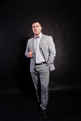 Studio portrait of man in gray suit and bow tie showing thumb up against black background.