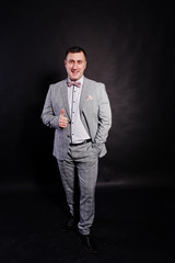 Studio portrait of man in gray suit and bow tie showing thumb up against black background.
