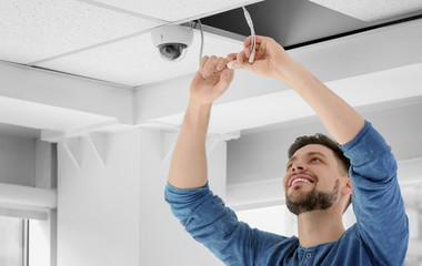 Technician installing CCTV camera on ceiling indoors
