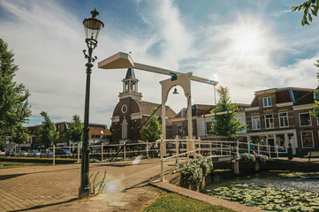 Bascule bridge over the canal with aquatic plants and houses on the sunlight in Weesp. Quiet and pleasant village full of canals and green near Amsterdam. Northern Netherlands. Retouched photo