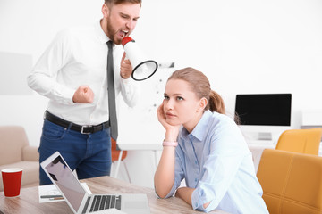 Angry boss with megaphone screaming at employee in office