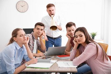 Angry boss with megaphone screaming at employees in office