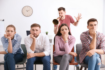 Angry boss with megaphone screaming at employees in office