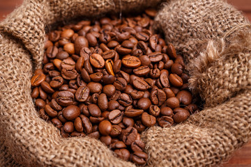 Fototapeta premium coffee beans in jute bag on wooden table. Burlap sack full of coffee beans on wood table
