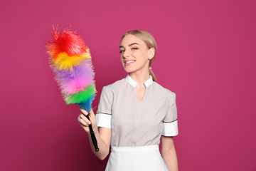 Young chambermaid with dusting brush on color background