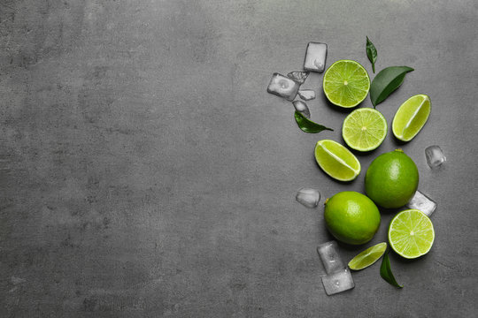 Fresh ripe limes and ice cubes on gray background, top view