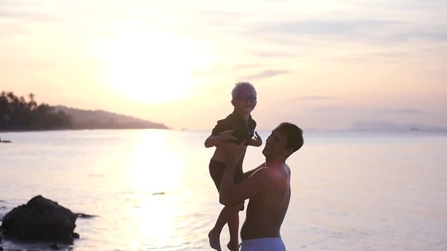 Father throws his adult son up, against the background of a beautiful sunset at sea. slow motion, 1920x1080, full hd