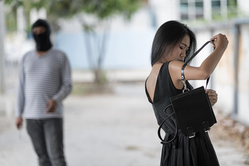 A woman is look at her bag. She do not beware. Blur background is a masked robber. is standing and look at a woman. Selective focus at a woman.