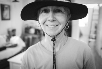 Cute older woman with sun hat on in a out of focus tropical inspired interior B&W film look