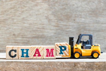 Toy forklift hold letter block P to complete word champ on wood background