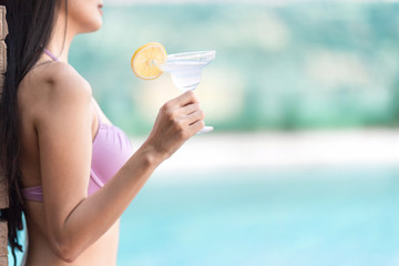 Sexy woman in bikini enjoy her cocktail at swimming pool with blurred background.