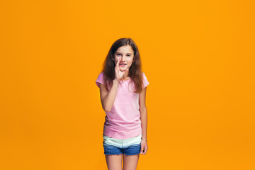 Obraz premium The young teen girl whispering a secret behind her hand over orange background