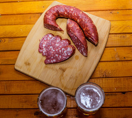 Two glasses of beer and sausage on a wooden table. The view from the top.