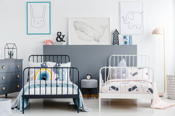 Grey stool between black and white bed in children bedroom interior with posters. Real photo