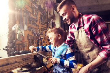 family, carpentry, woodwork and people concept - happy father and little son with rasp grinding wood plank at workshop