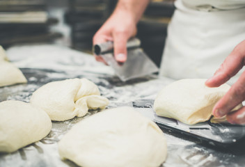 Hands of a male baker measuring pieces of wheat dough for bread or pizza