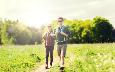 travel, hiking, backpacking, tourism and people concept - happy couple with backpacks and walking along country road outdoors