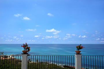 Blick von einer Terrasse in Tropea auf das Mittelmeer mit Strand, Häusern Blumen und Palmen