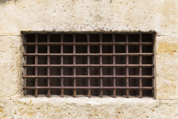 old window in a medieval castle protected by a rusty iron grating with spikes
