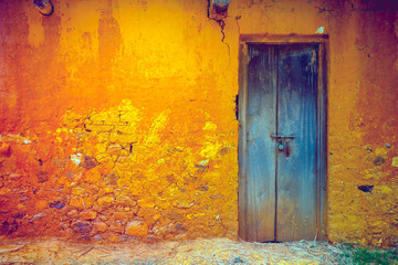 Stylish cracked vintage colorful wall in yellow orange shades with royal blue wooden door. Ideal background for retro style illustrations and collages. Grunge style. Artistic retouching.