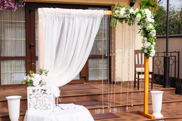 beautiful arc is decorated with white tulle, flowers and chains of transparent beads. A table with a gift box on the background of the restaurant